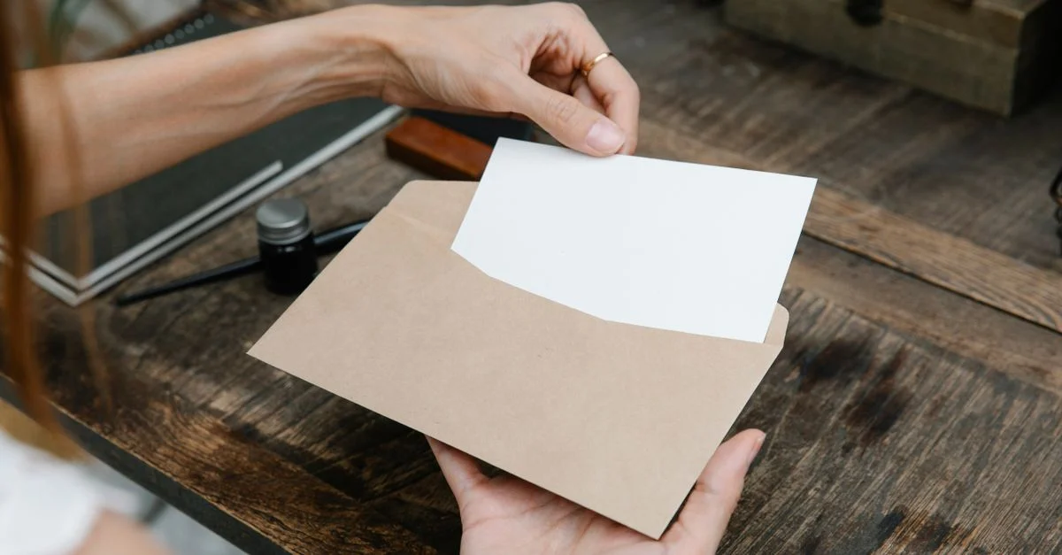Gros plan de mains tenant une enveloppe avec une lettre sur un bureau en bois rustique, idéal pour des thèmes de communication.