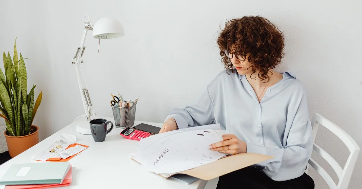 Femme examinant des documents dans son bureau à domicile avec une plante et une lampe.