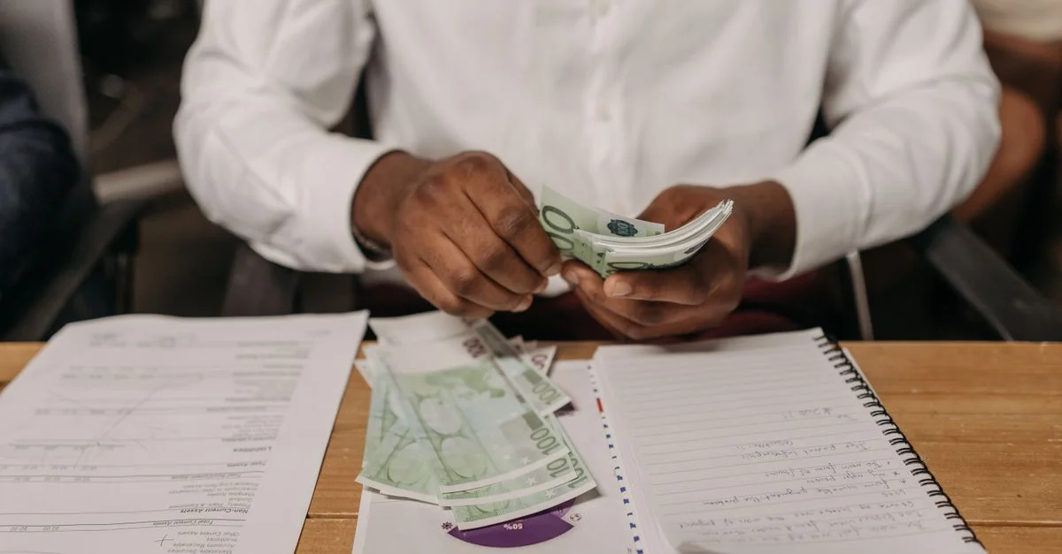 Homme d'affaires africain comptant des billets en euros à un bureau avec des documents et un carnet, mettant en avant le thème de la finance.