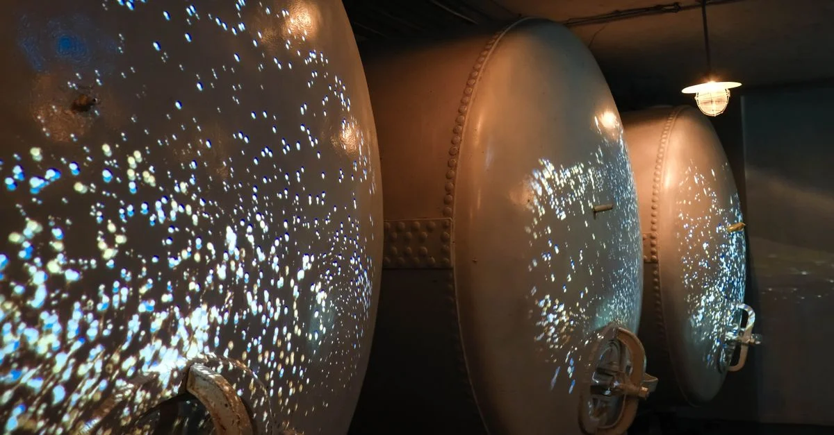 Des cuves de fermentation industrielles faiblement éclairées, aux reflets lumineux uniques, créent une atmosphère futuriste.