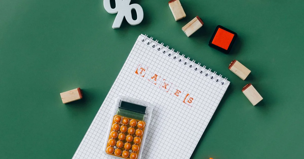 Vue de dessus des essentiels fiscaux avec calculatrice, carnet et tampons sur un fond vert.