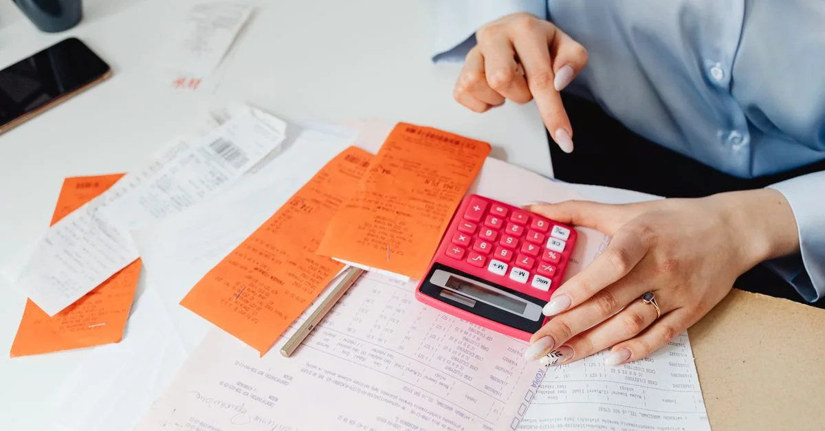 Une femme d'affaires calcule ses dépenses en utilisant des reçus et une calculatrice à son bureau. Idéal pour des thèmes de finance et de comptabilité.