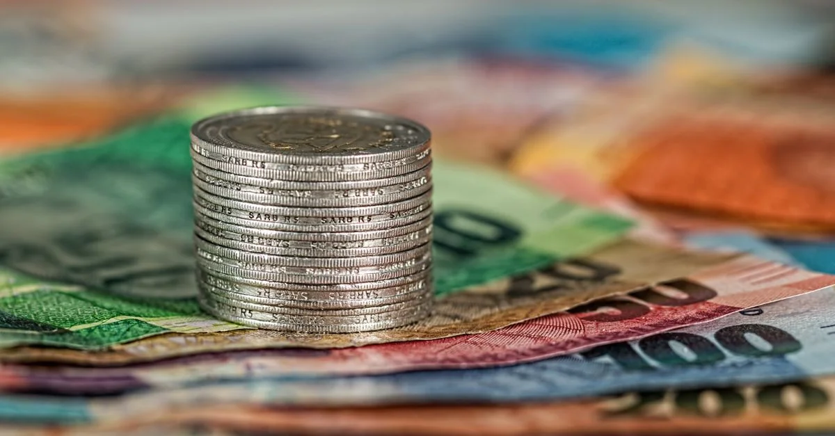 Une pile de pièces sur des billets de banque colorés, symbolisant la finance et la monnaie.