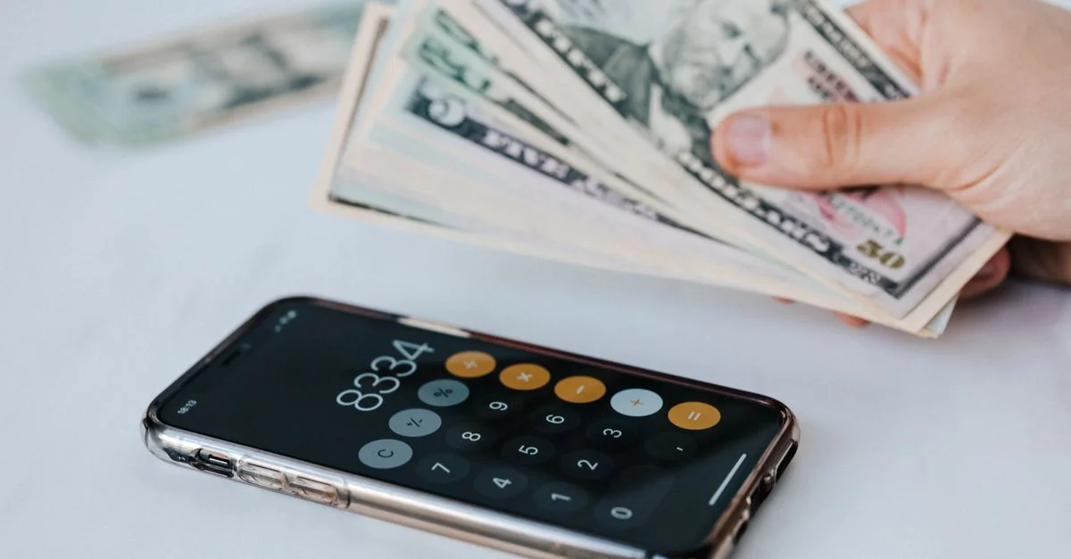 Main tenant des billets de dollar avec l'application calculatrice du smartphone affichant 8334.