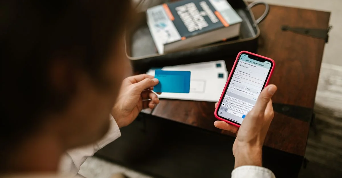 Personne effectuant un paiement en ligne avec un smartphone et une carte de crédit à l'intérieur.