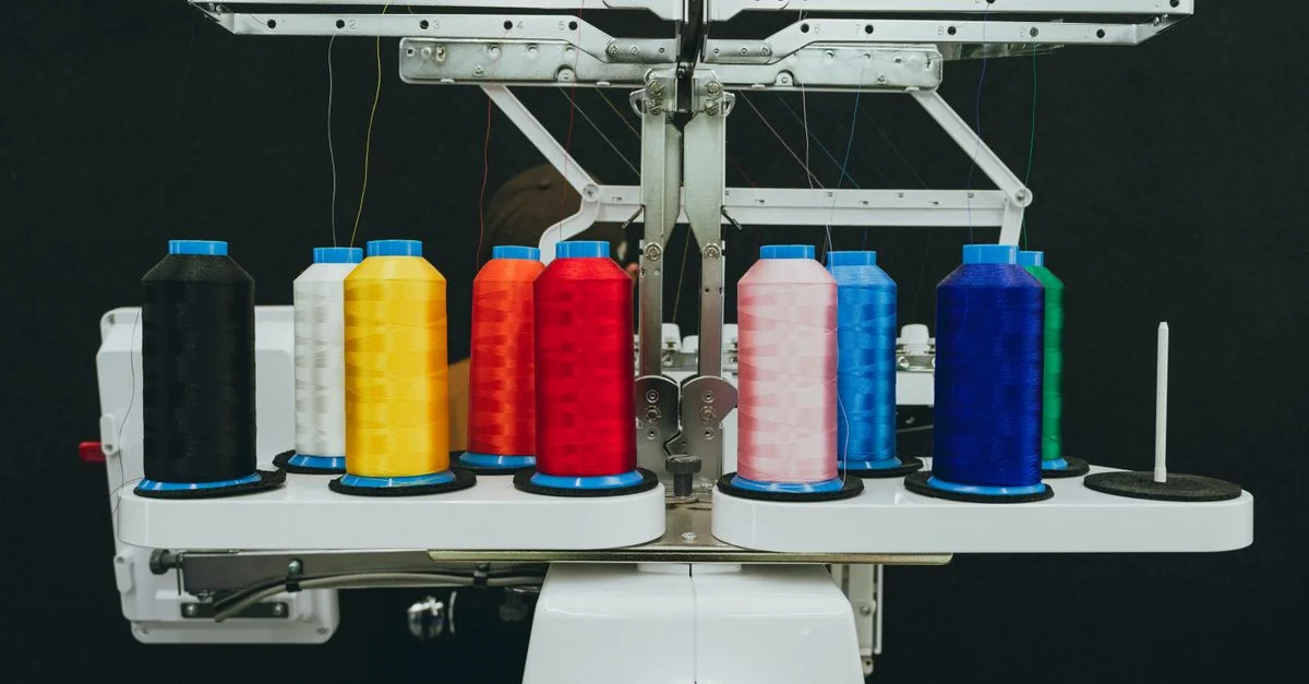 Gros plan sur des bobines de fil colorées sur une machine à broder industrielle dans un atelier textile.