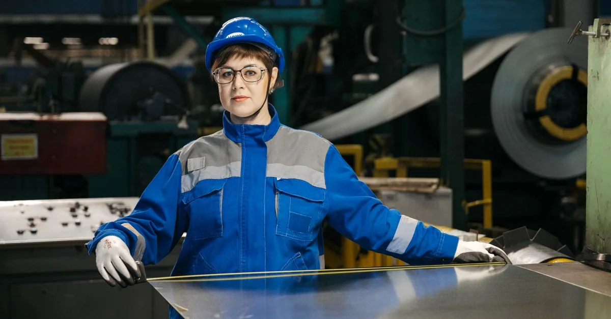 Ouvrière d'usine en tenue de protection manipulant une tôle en milieu industriel. Orientation sécurité et industrie.