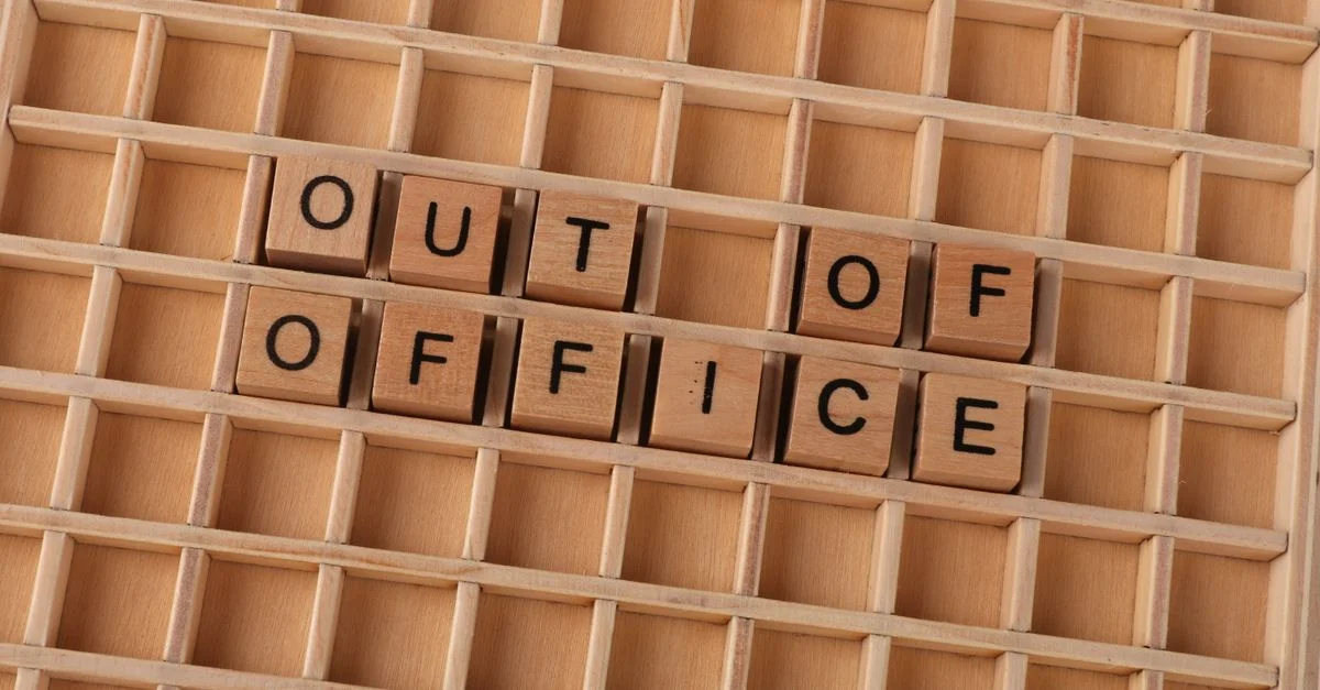 Des lettres en bois forment le mot « Absent du bureau » sur un fond de grille en bois.