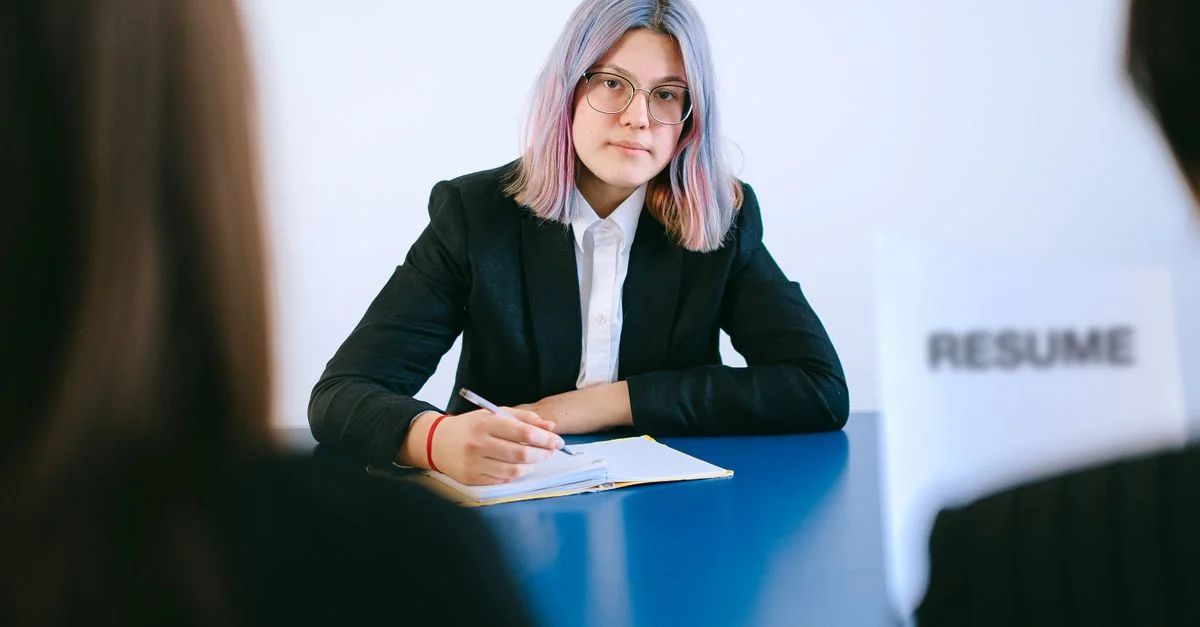 Une jeune femme aux cheveux teints prend des notes lors d'un entretien d'embauche.