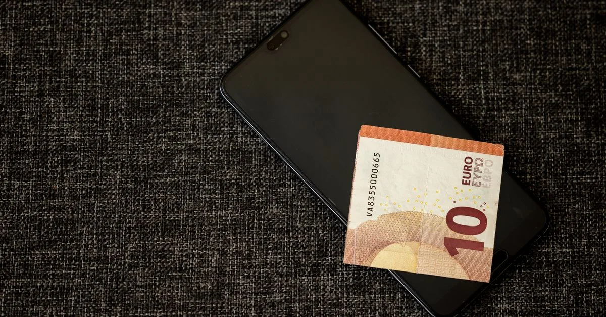 Un billet de 10 euros posé sur un smartphone sur un fond en tissu texturé sombre.