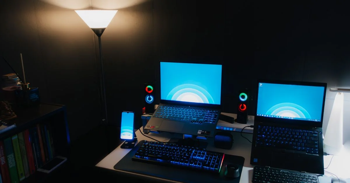 Configuration de bureau de nuit avec des ordinateurs portables, clavier éclairé et éclairage ambiant.