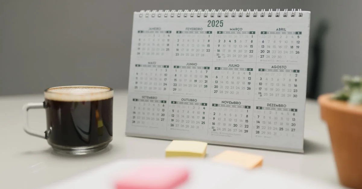 Un calendrier 2025 sur un bureau avec du café, des notes autocollantes et une plante dans un environnement de bureau.