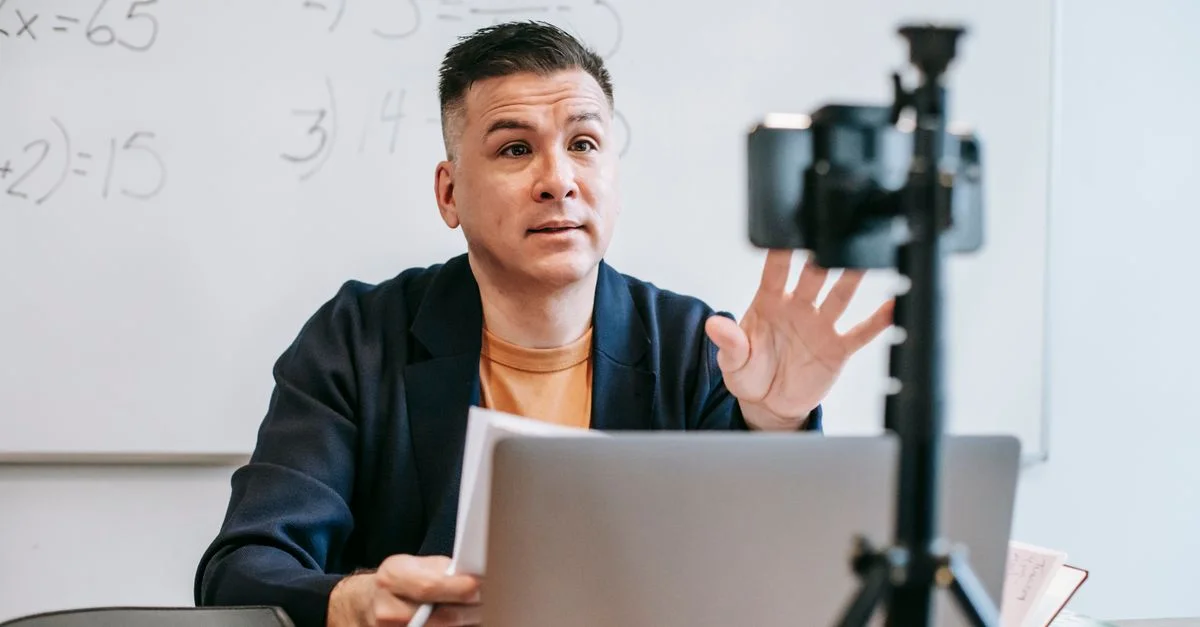 Un instructeur masculin animant une session d'enseignement en ligne à l'aide d'un ordinateur portable et d'une caméra.