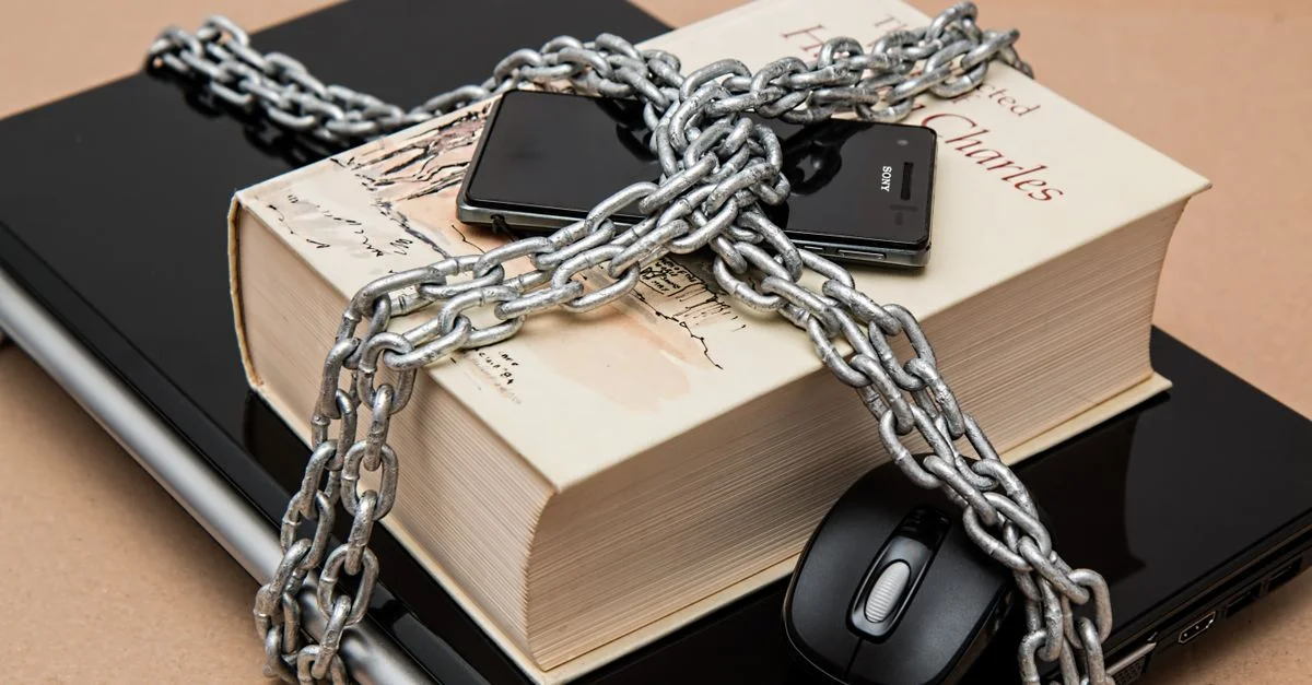 Livre verrouillé par une chaîne, téléphone et ordinateur portable symbolisant la sécurité numérique et intellectuelle.