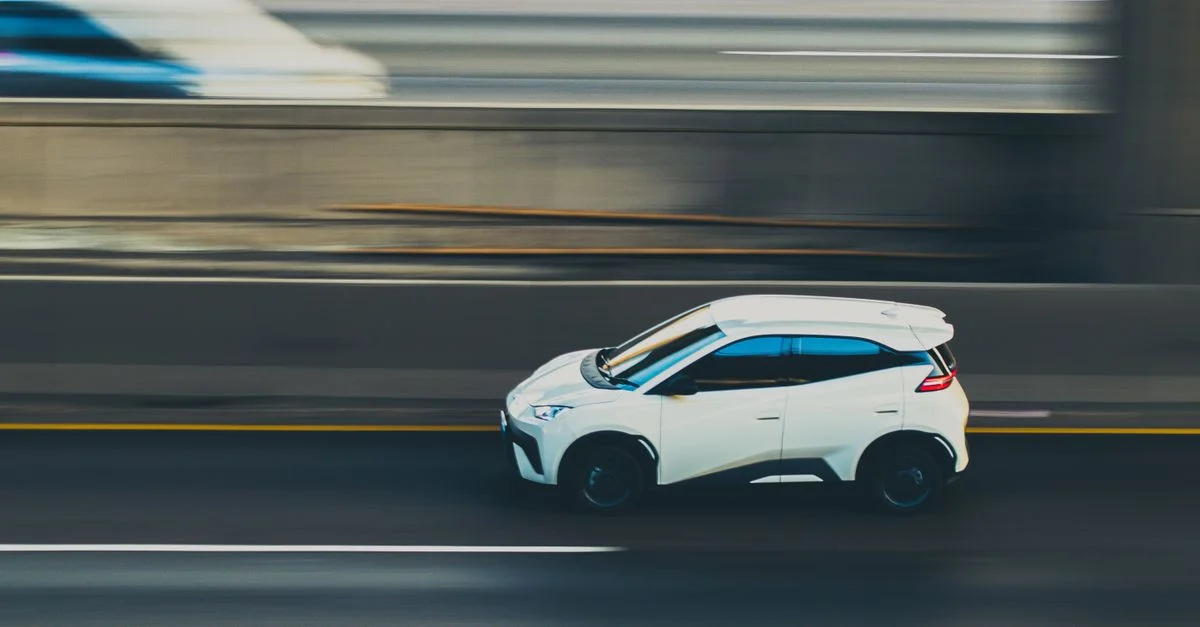Plan panoramique à grande vitesse capturant une voiture blanche en mouvement sur une autoroute, mettant en évidence la vitesse et le mouvement.