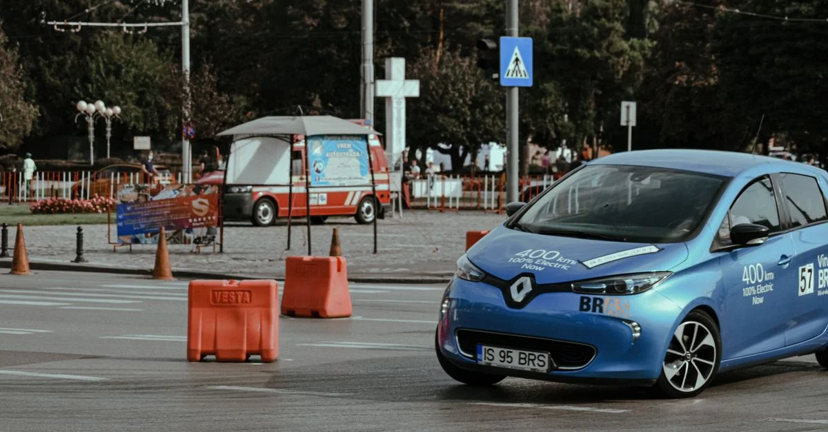 Voiture électrique bleue naviguant dans une rue de la ville marquée par des cônes de circulation.