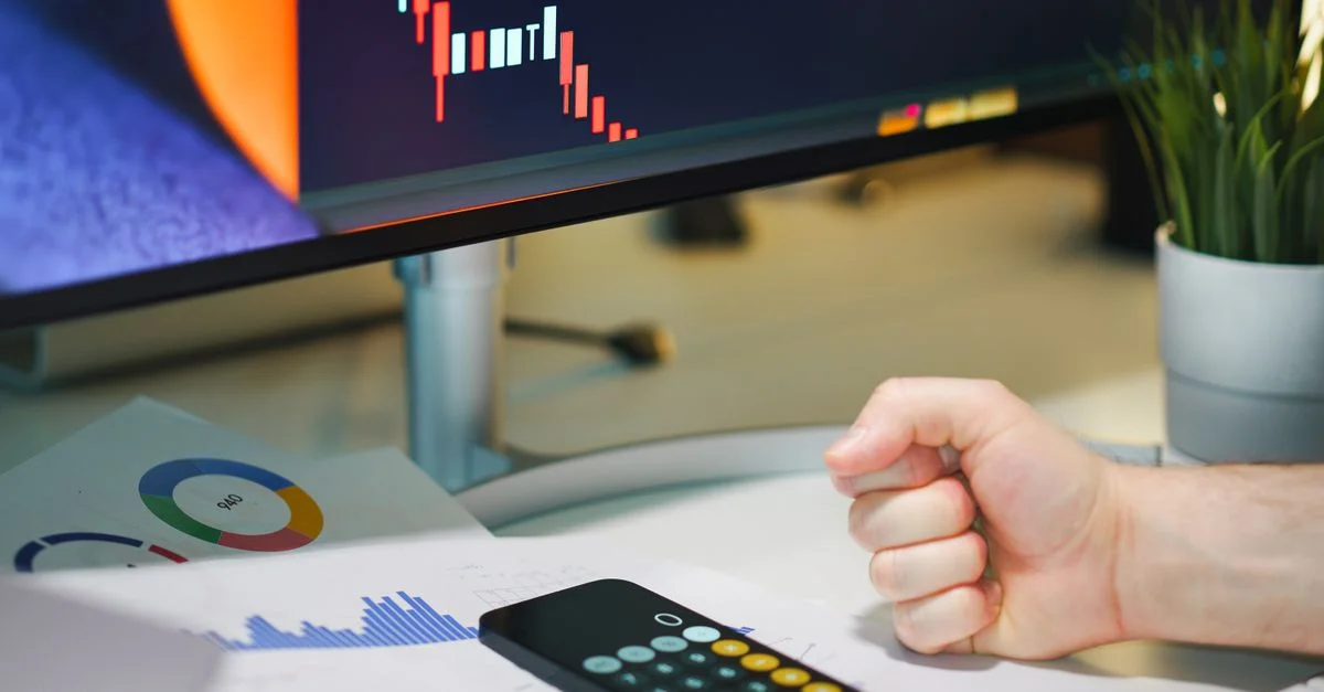 Gros plan d'un bureau avec des graphiques financiers, une calculatrice et un poing symbolisant la détermination.