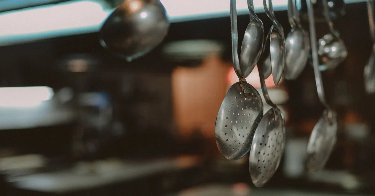 Gros plan sur des cuillères et louches en métal suspendues dans une cuisine, arrière-plan flou