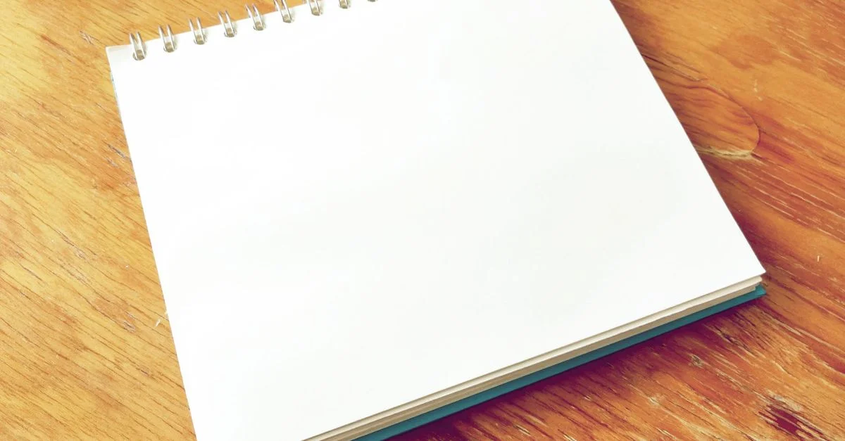 Un carnet à spirale vierge est ouvert sur un bureau en bois, parfait pour prendre des notes ou faire des croquis.