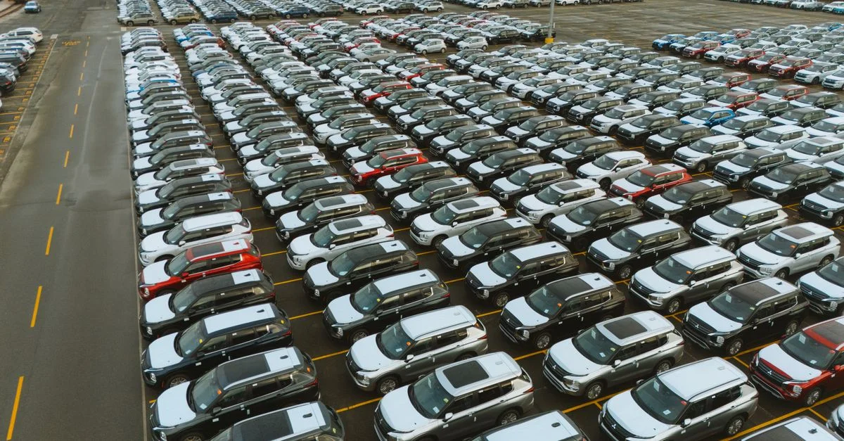 Vue aérienne d'un vaste parking rempli de véhicules neufs prêts à être distribués.