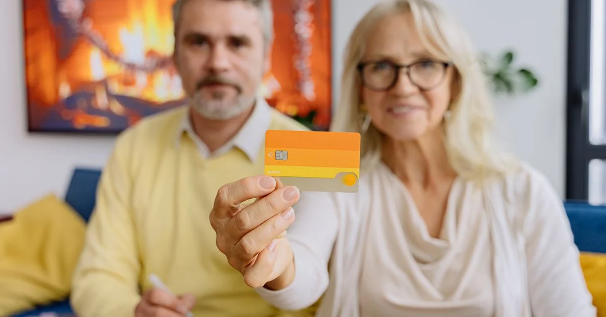Un couple âgé dans un salon chaleureux tenant une carte de crédit, symbolisant la banque moderne.
