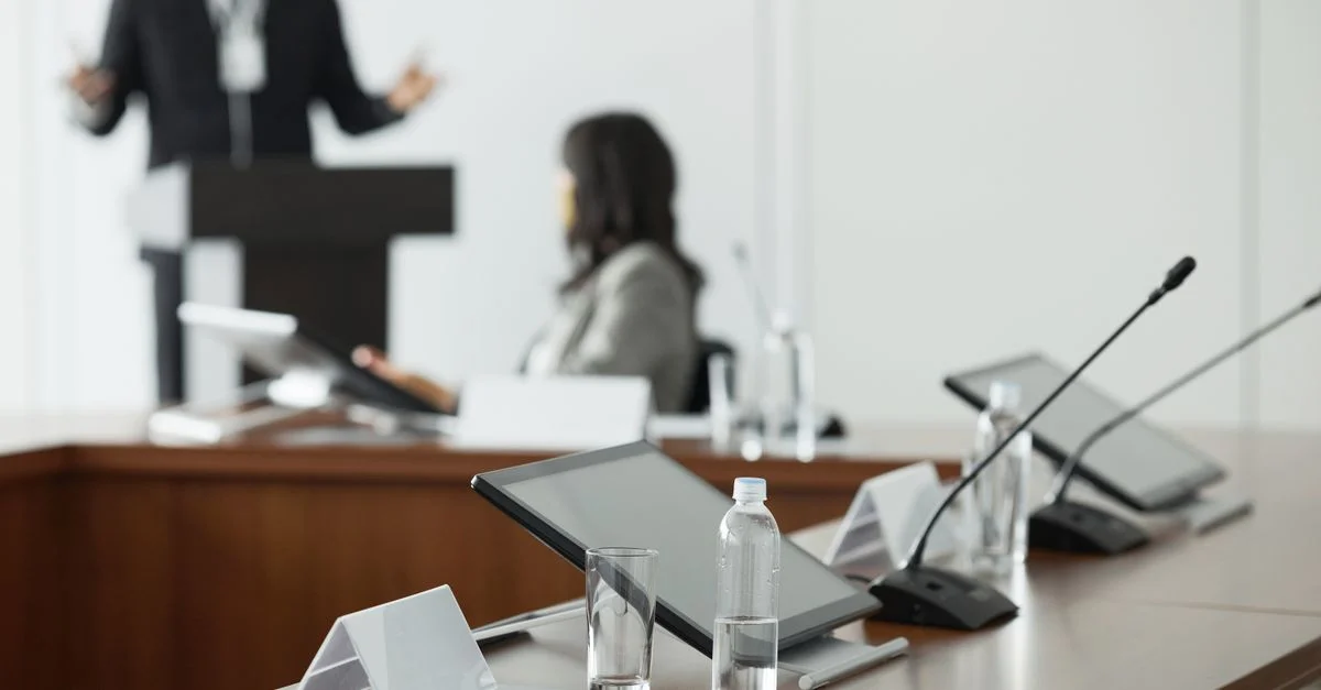 Une configuration de salle de conférence avec des tablettes, des microphones et des bouteilles d'eau pour une réunion professionnelle.