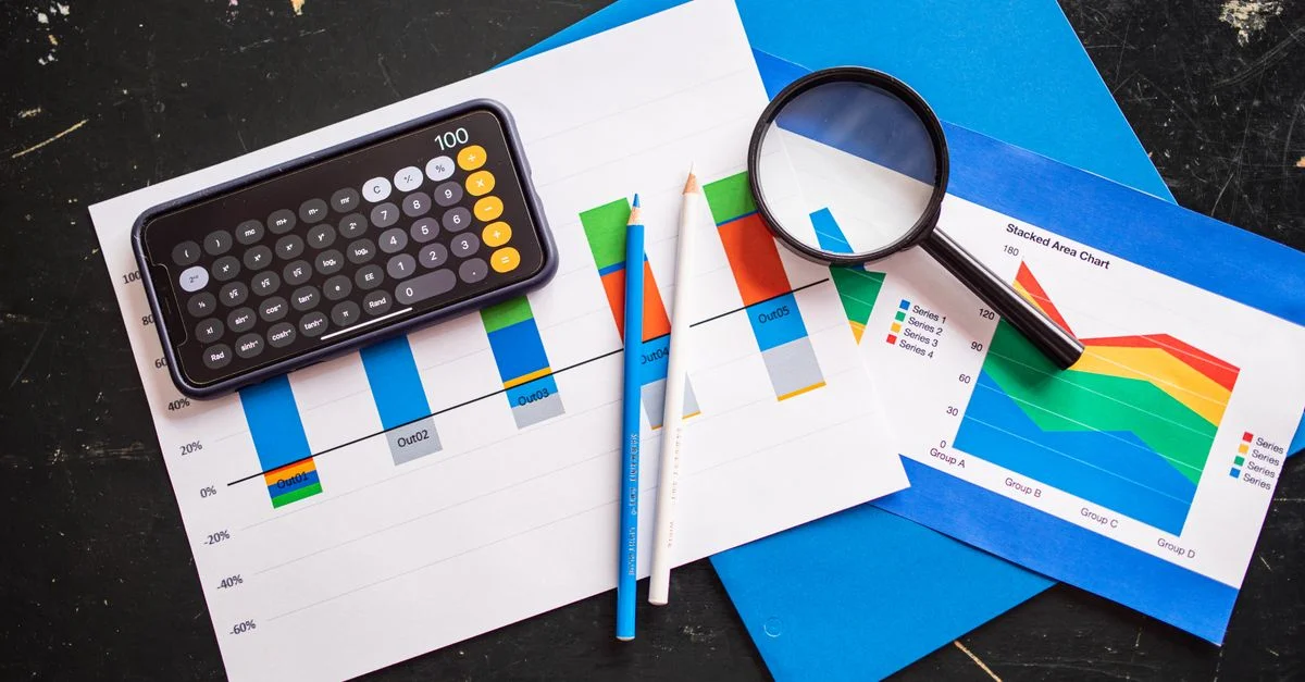 Vue de dessus de graphiques financiers avec une calculatrice smartphone, une loupe et des crayons sur un bureau.