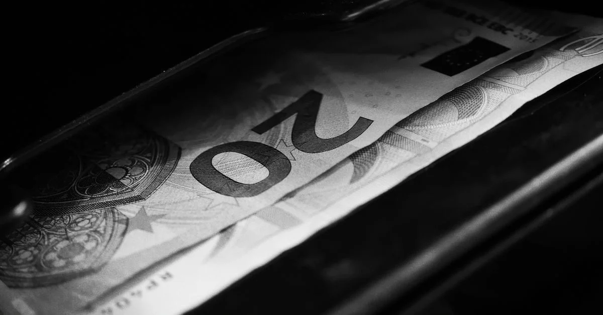 Image en noir et blanc mettant en évidence un billet de 20 euros dans une caisse enregistreuse, illustrant des concepts financiers.