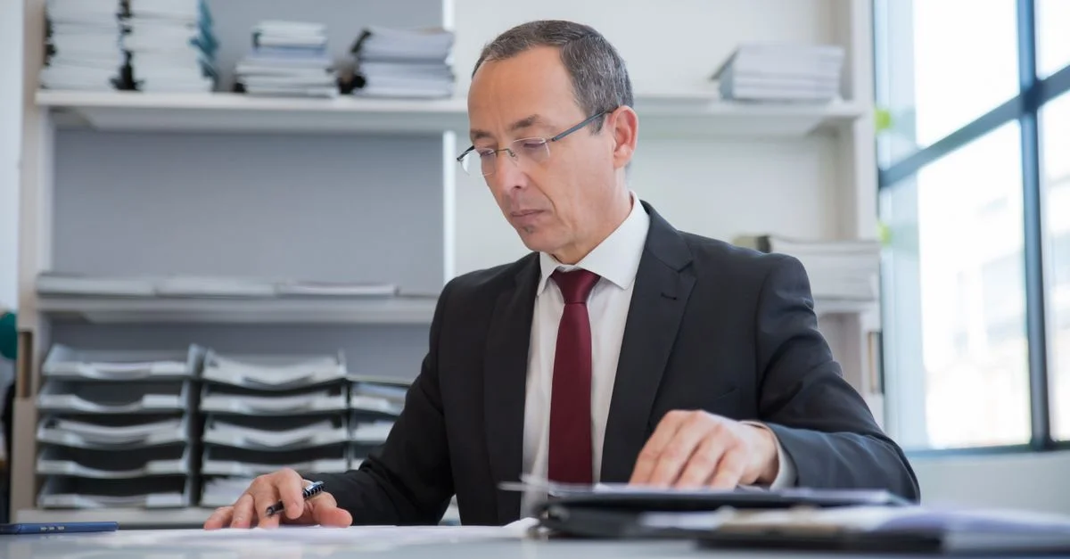 Un homme d'affaires dans un cadre formel examinant des documents à un bureau.