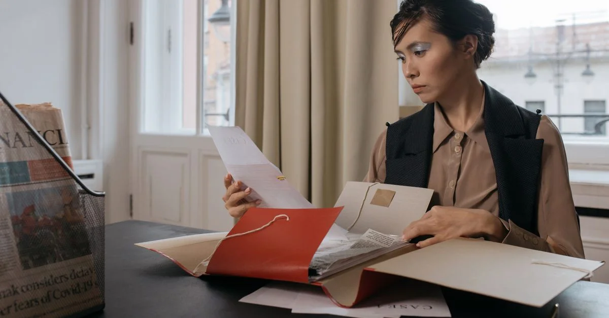 Femme d'affaires dans un bureau examinant des documents importants d'un dossier rouge avec concentration et détermination.