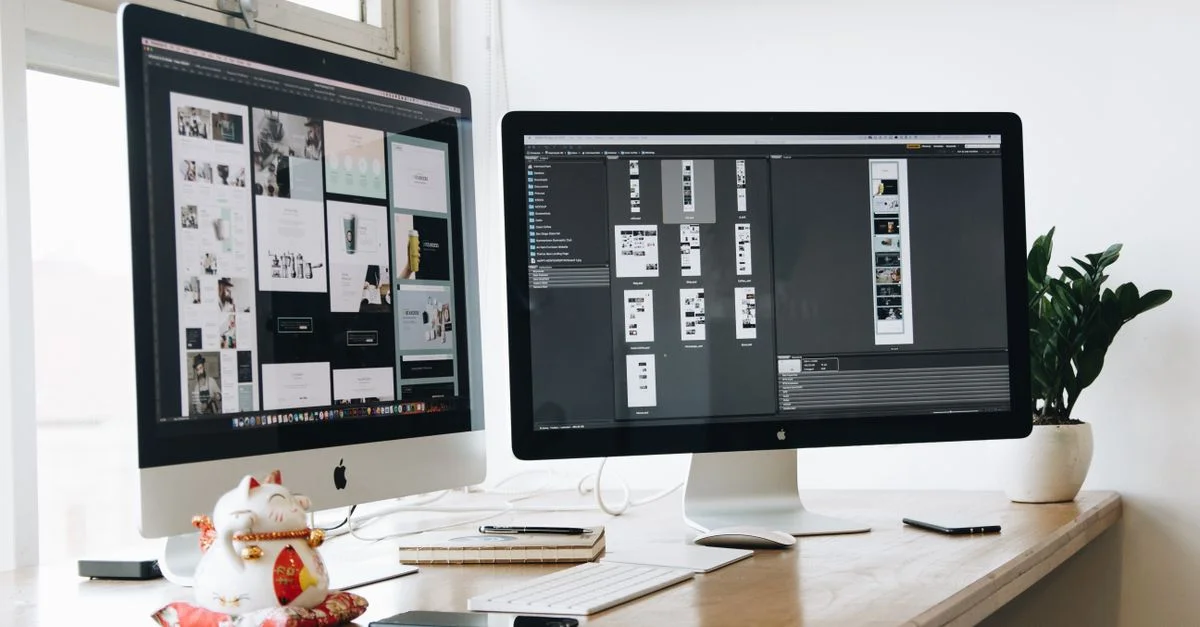 Espace de travail élégant avec des moniteurs doubles sur un bureau en bois, présentant une plante et une décoration de chat porte-bonheur.