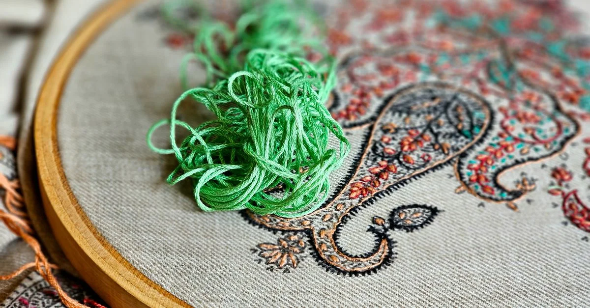 Gros plan sur une broderie au fil vert sur un tissu à motif cachemire, dans un tambour à broder.