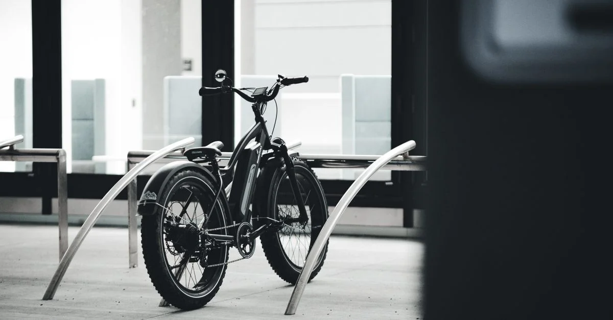 Image en noir et blanc d'un vélo électrique garé à l'intérieur dans un environnement urbain.