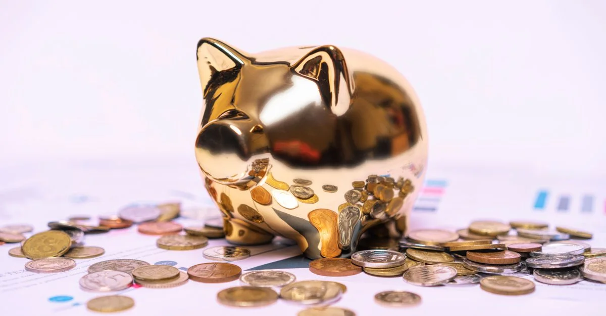 Tirelire dorée brillante sur des documents financiers avec des pièces éparpillées symbolisant l'épargne.