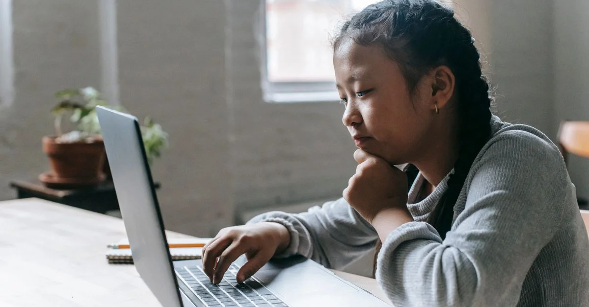 Une jeune fille étudie attentivement en ligne chez elle en utilisant son ordinateur portable, incarnant l'éducation moderne.