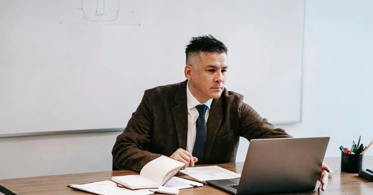 Homme en costume travaillant sur un ordinateur portable avec des documents dans un bureau moderne.
