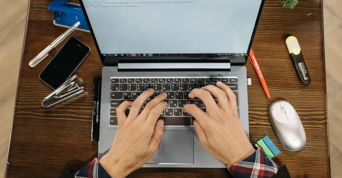 Vue de dessus des mains tapant sur un ordinateur portable, entourées de fournitures de bureau sur un bureau en bois.