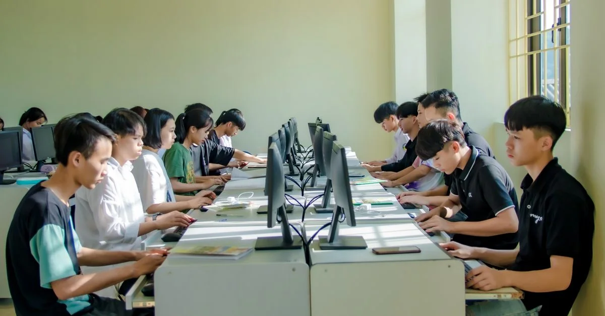 Un groupe d'étudiants dans une salle de classe concentré sur des écrans d'ordinateur, favorisant l'éducation numérique.