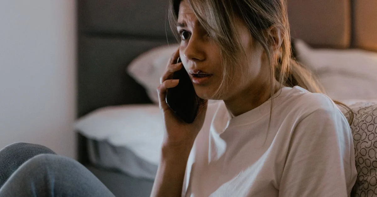 Une femme inquiète en chemise blanche faisant un appel téléphonique angoissant à l'intérieur.