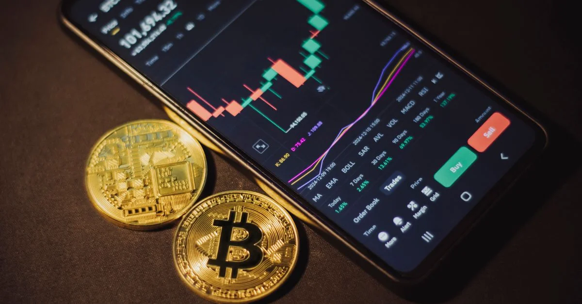 Smartphone affichant une application de trading avec des pièces Bitcoin sur une surface sombre.
