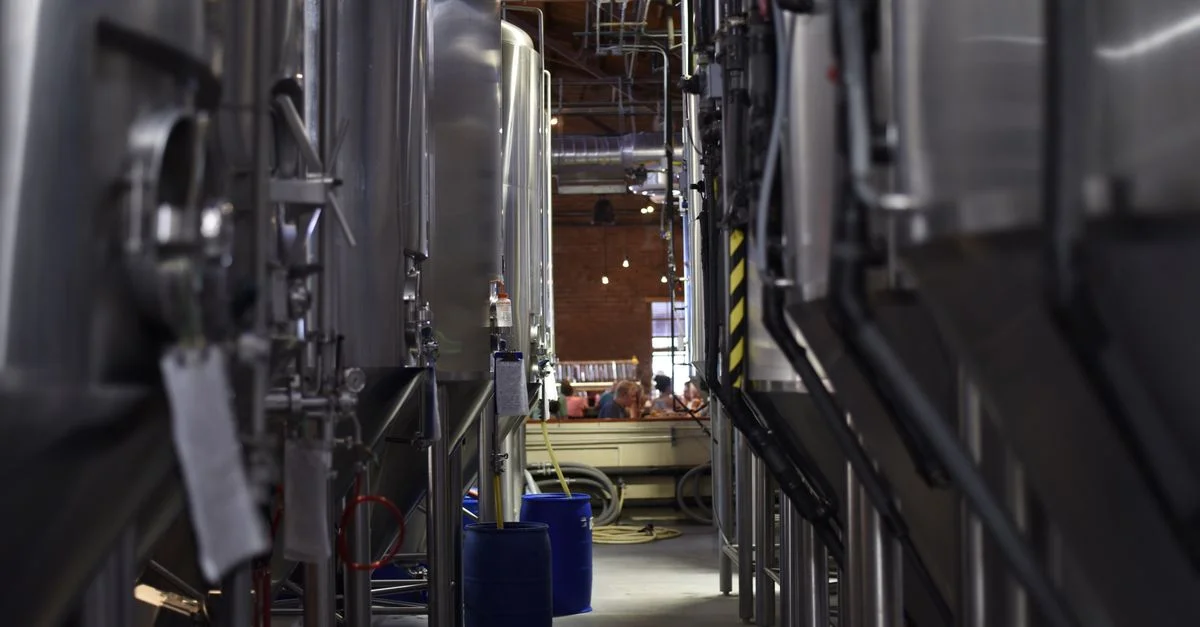 Vue intérieure d'une brasserie moderne avec de grandes cuves en acier inoxydable et des machines pour la production de bière.