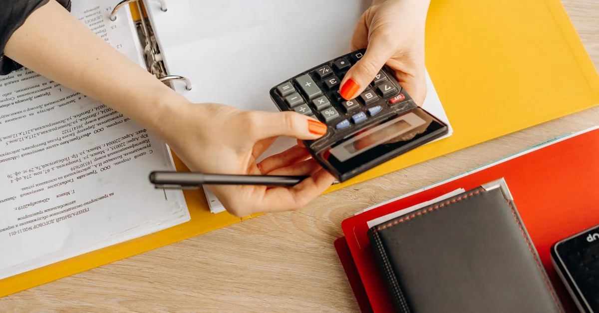 Mains utilisant une calculatrice sur un bureau avec des documents et des dossiers, idéal pour des thèmes de finance ou de comptabilité.