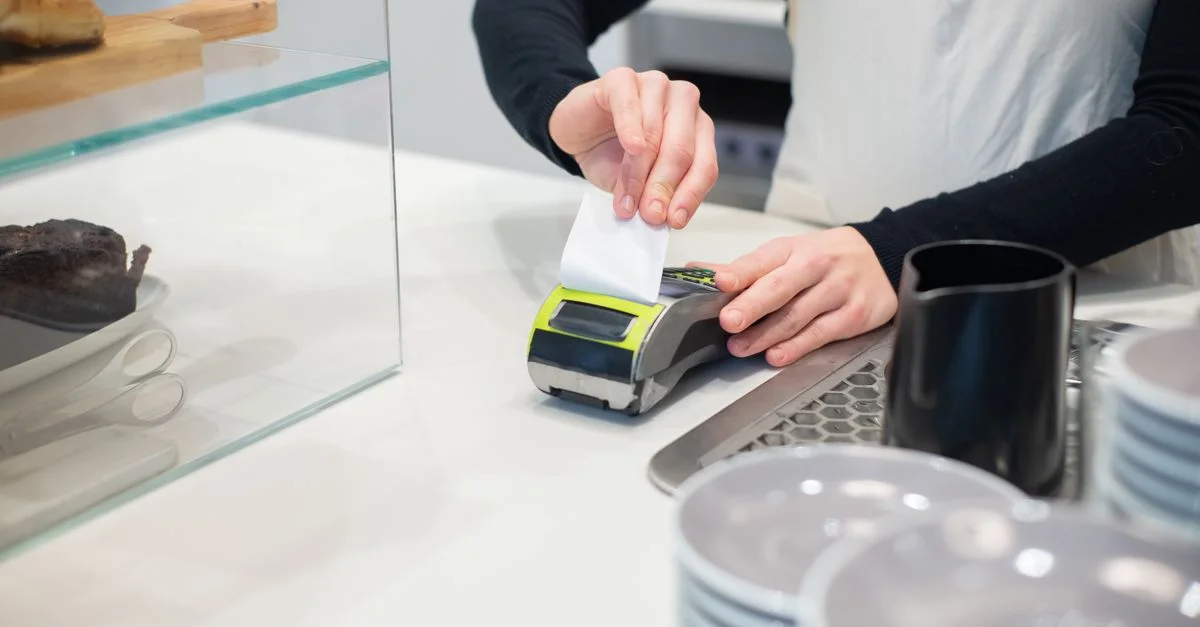 Gros plan sur une transaction sans espèces au comptoir d'un café moderne avec des mains tenant un reçu.