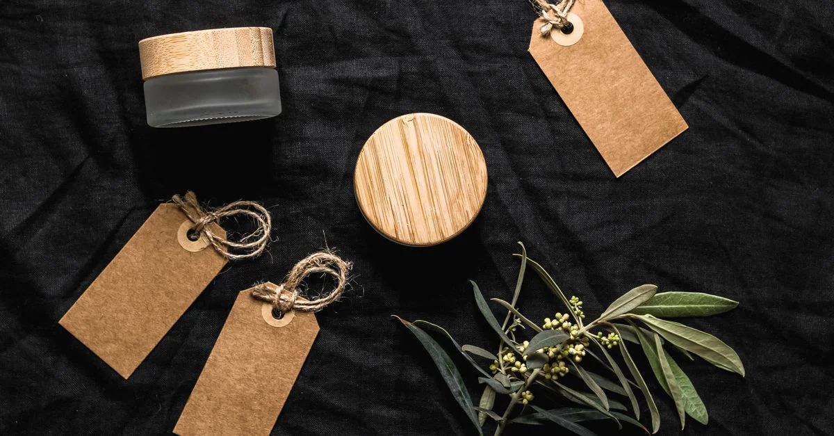 Vue de dessus de pots cosmétiques écologiques, d'étiquettes et de feuilles sur un tissu noir pour une esthétique durable.