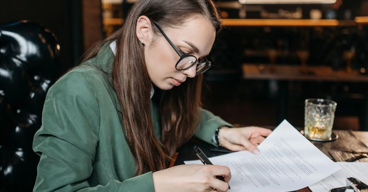 Femme d'affaires concentrée en tenue verte signant des documents importants à son bureau.