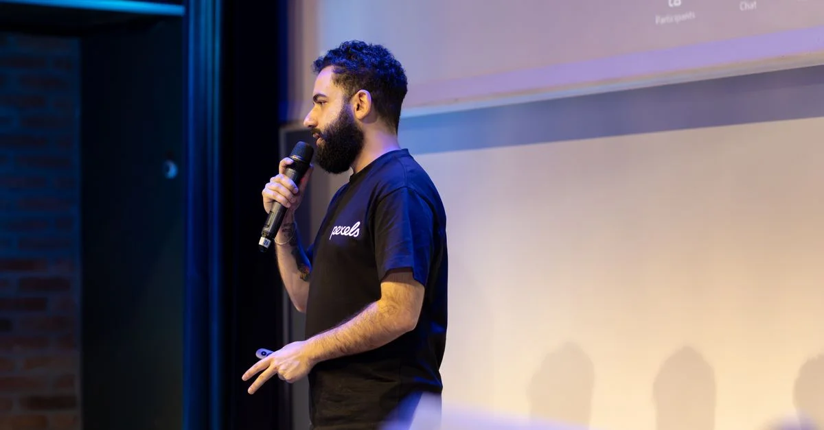 Un homme parle au microphone lors d'une présentation à l'intérieur.