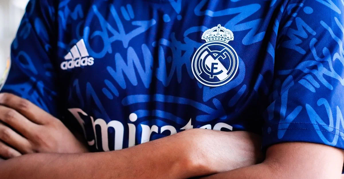 Les bras croisés dans un maillot de sport bleu vif avec logo d'équipe et design à motif abstrait.