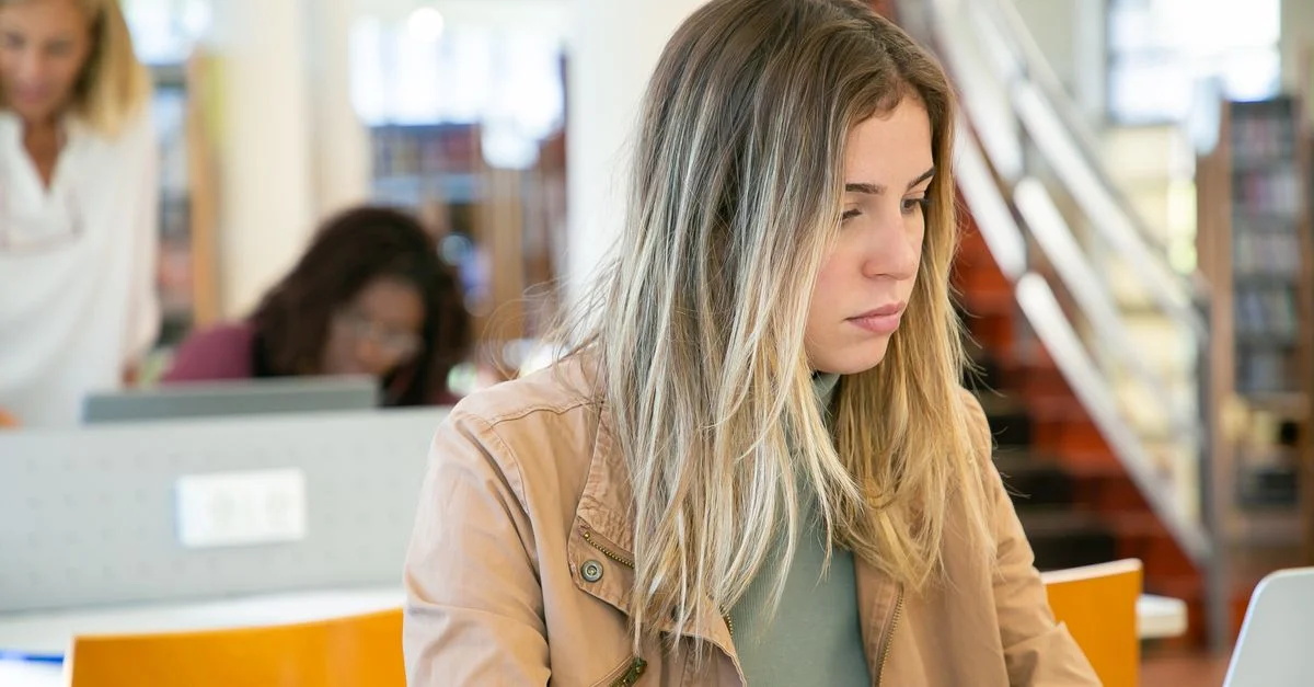 Jeune femme étudiant sur un ordinateur portable dans une bibliothèque universitaire, se concentrant profondément sur son travail.