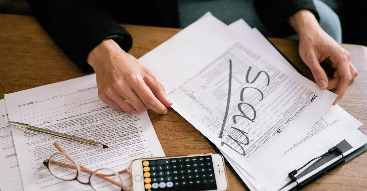 Mains d'une personne examinant des formulaires fiscaux étiquetés comme une arnaque avec une calculatrice et des papiers.