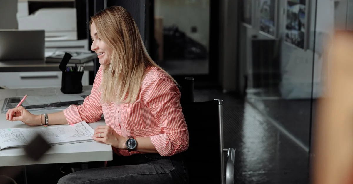 Femme professionnelle assise à son bureau, travaillant dans un environnement de bureau lumineux.